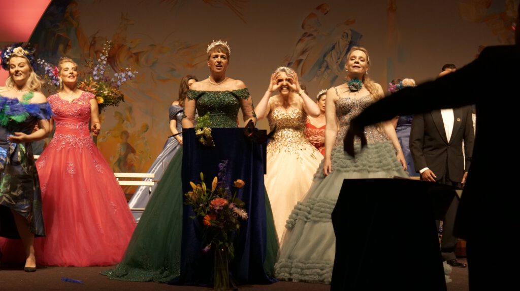 Zangeressen in theatrale avondjurken brengen een speelse operettepassage ten gehore met kleurrijk decor op de achtergrond.