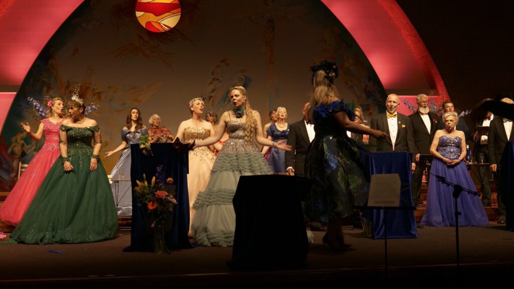 Koorleden zingen in kooropstelling onder een kleurrijk gewelf tijdens het operette-openingsconcert van Wilhelmina.