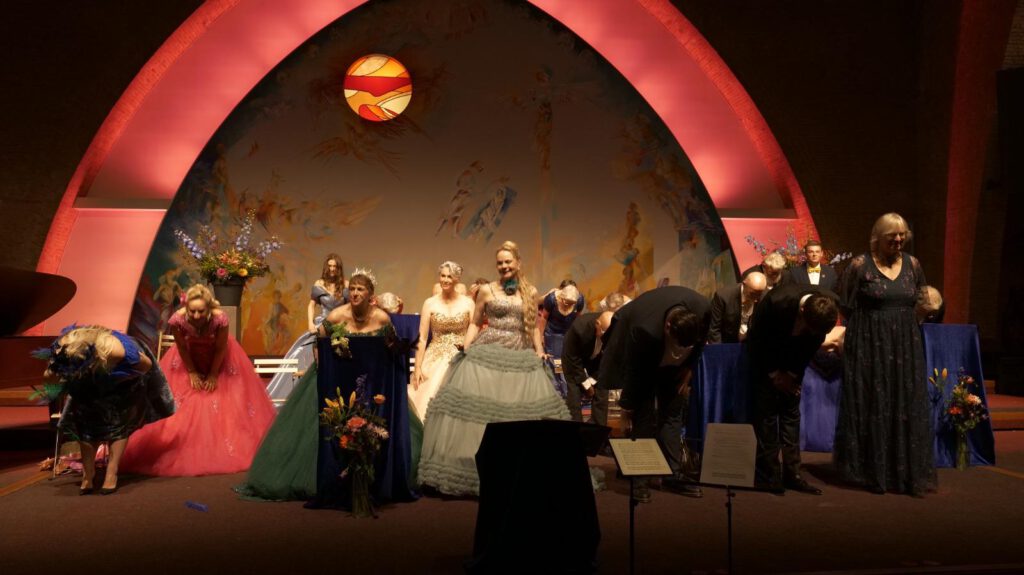 Slotmoment van het concert: koorleden buigen voor het publiek in de sfeervol verlichte Sacramentskerk in Breda.